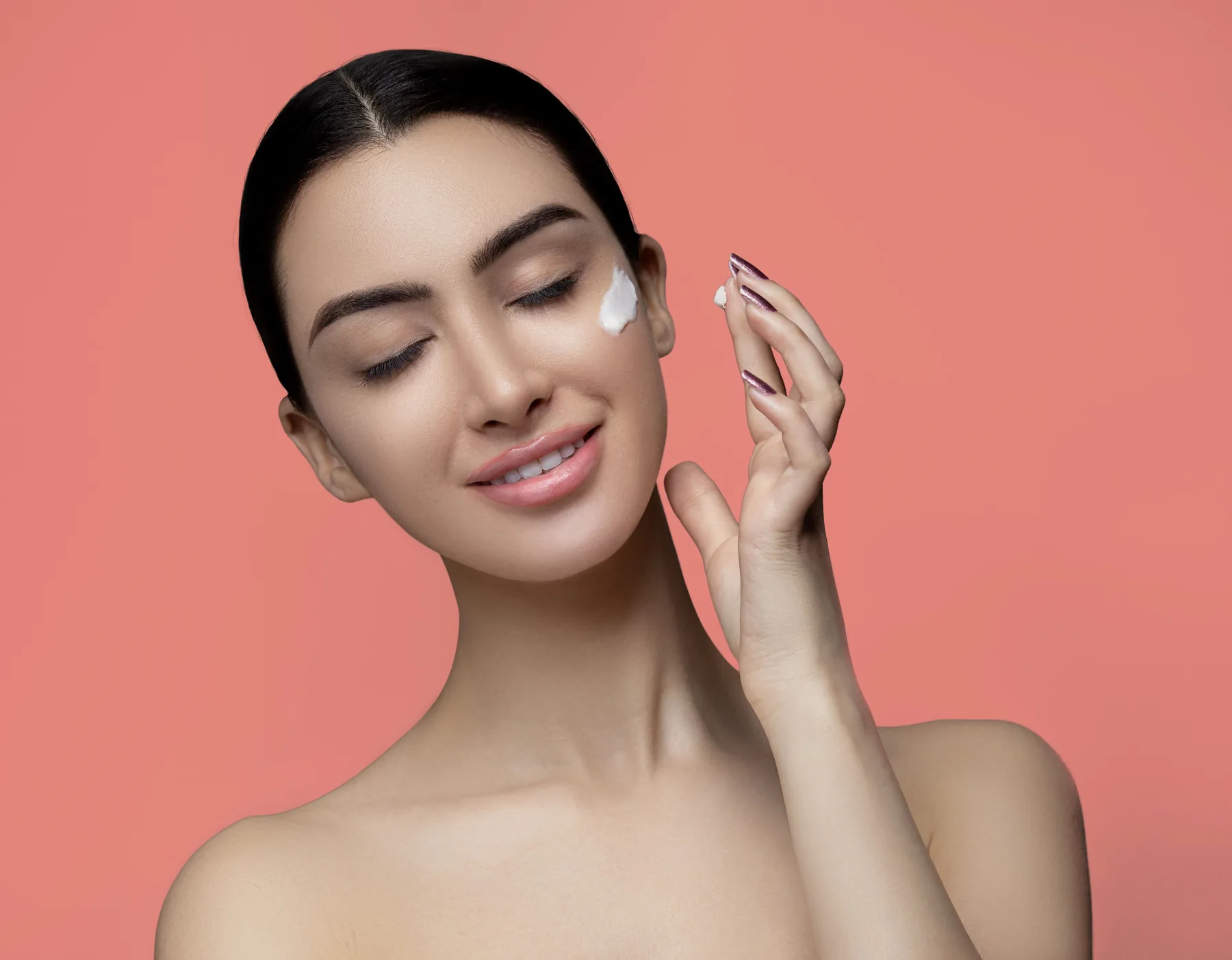 Woman applying skincare cream against a soft pink background
